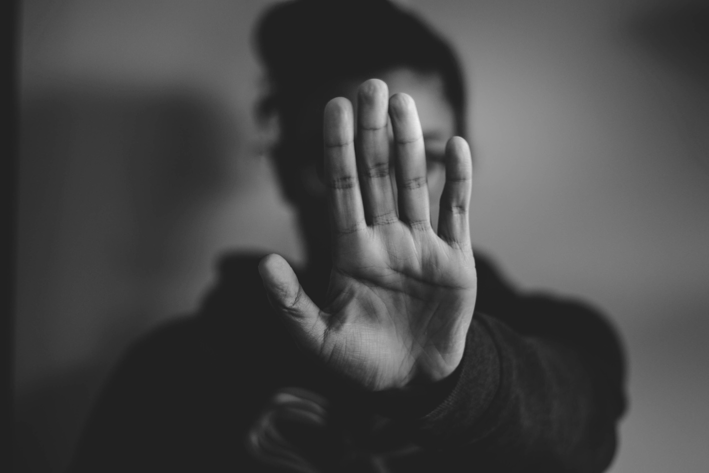 Portrait noir et blanc d'une personne cachant son visage avec sa main. Interprétable comme un signe de refus.